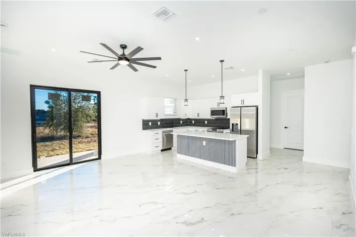 Kitchen featuring decorative light fixtures, white cabinetry, a center island, appliances with stainless steel finishes, and light marble finish flooring