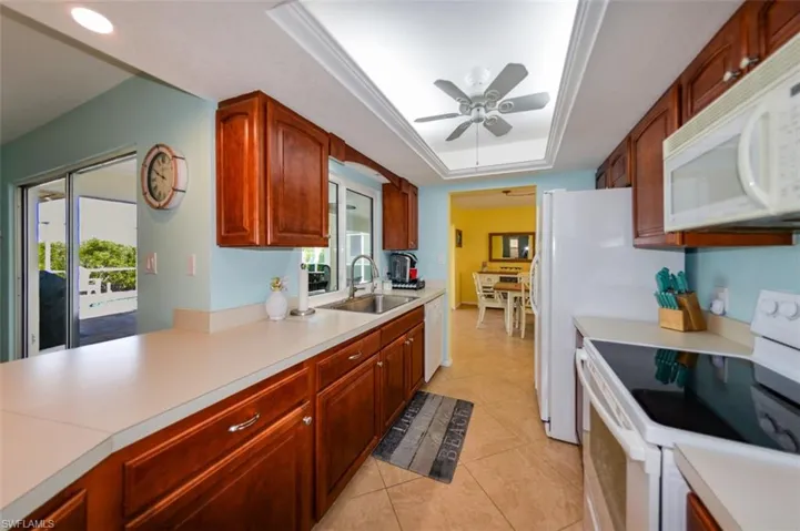 Kitchen with ceiling fan, sink, white appliances, and a healthy amount of sunlight