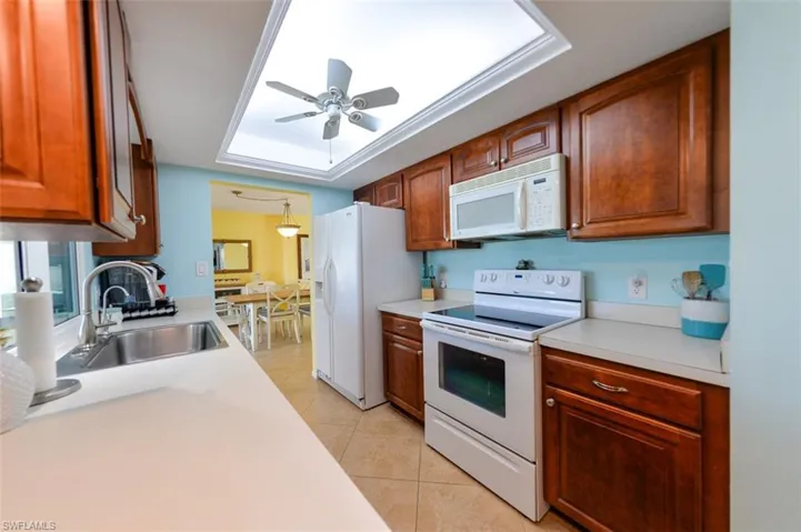 Kitchen with white appliances, a tray ceiling, sink, and ceiling fan