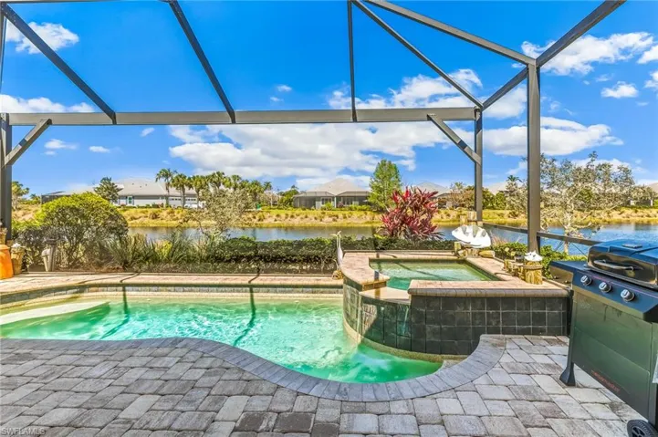 Combined pool / hot tub featuring glass enclosure, a grill, a sunroom, a patio area, and a water view