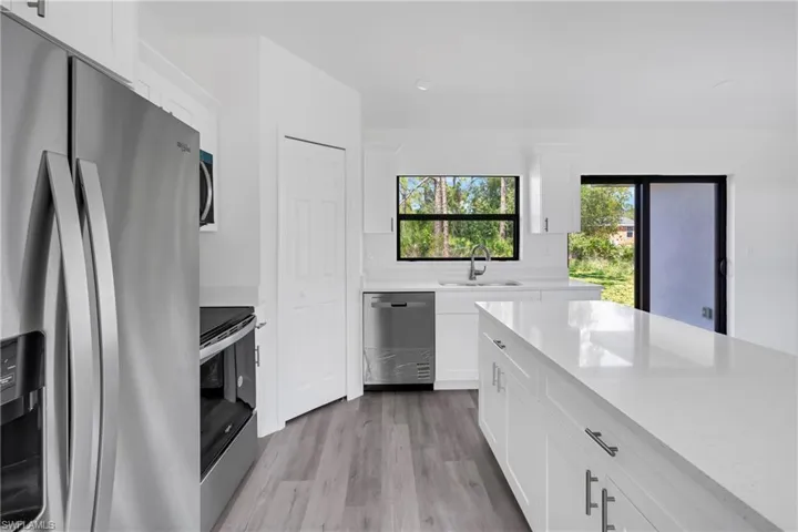 Kitchen with stainless steel appliances, white cabinets, light wood-type flooring, and light stone countertops