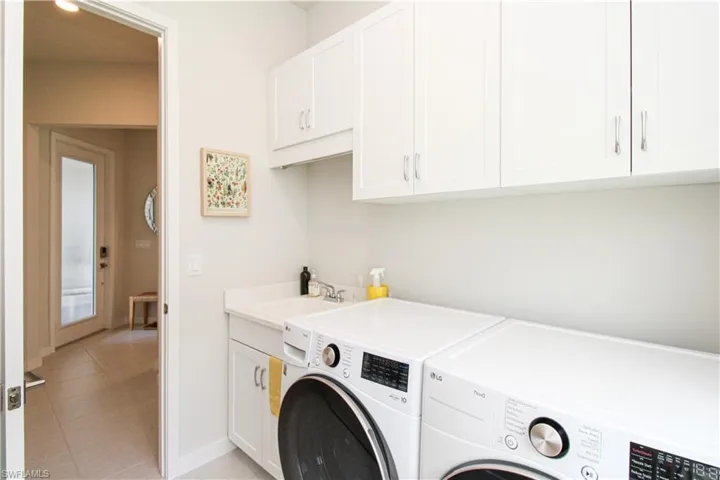 Washroom with light tile patterned flooring, cabinets, washing machine and dryer, and sink