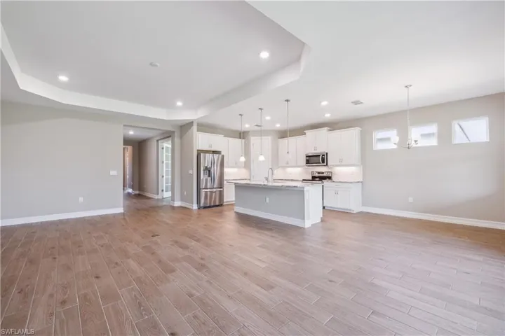 Kitchen featuring light hardwood / wood-style floors, decorative light fixtures, stainless steel appliances, an island with sink, and white cabinets