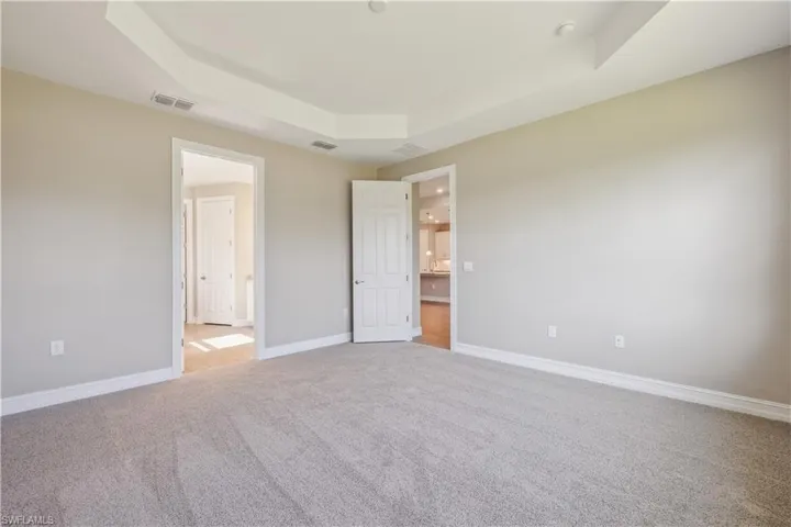 Unfurnished bedroom with a tray ceiling and light colored carpet