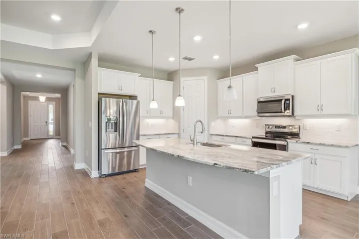 Kitchen featuring an island with sink, stainless steel appliances, white cabinets, sink, and light hardwood / wood-style flooring