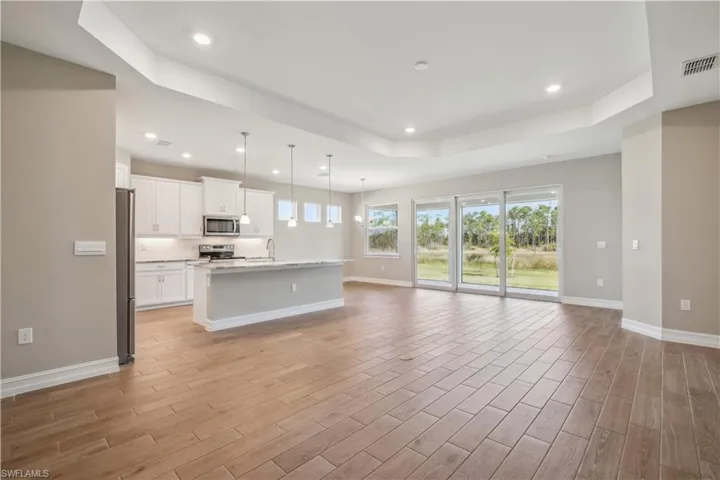 Kitchen featuring a kitchen island with sink, pendant lighting, light hardwood / wood-style flooring, stainless steel appliances, and white cabinetry