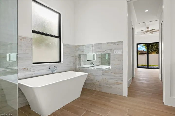 Bathroom featuring wood-type flooring, tile walls, a bathing tub, and ceiling fan