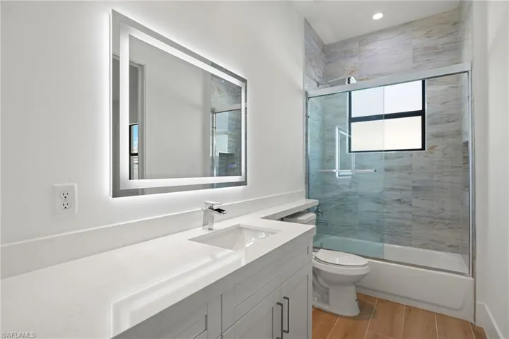 Full bathroom with hardwood / wood-style floors, vanity, toilet, and shower / bath combination with glass door