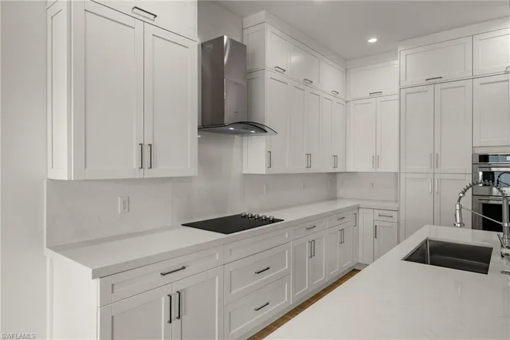 Kitchen with white cabinetry, sink, wall chimney exhaust hood, stainless steel double oven, and black electric cooktop