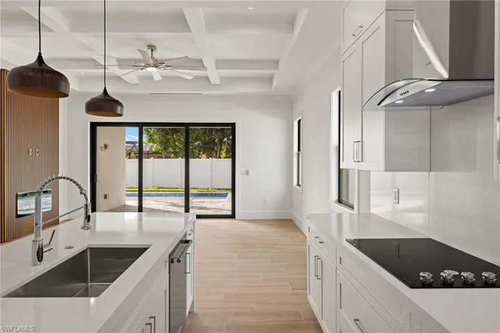 Kitchen with sink, white cabinetry, coffered ceiling, and wall chimney range hood