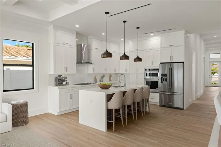 Kitchen featuring wall chimney range hood, sink, white cabinetry, a kitchen island with sink, and stainless steel appliances