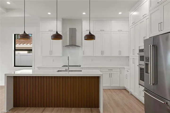 Kitchen with stainless steel appliances, a kitchen island with sink, pendant lighting, white cabinets, and light hardwood / wood-style floors