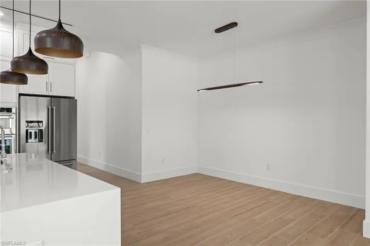 Kitchen with white cabinets, stainless steel appliances, decorative light fixtures, and light wood-type flooring