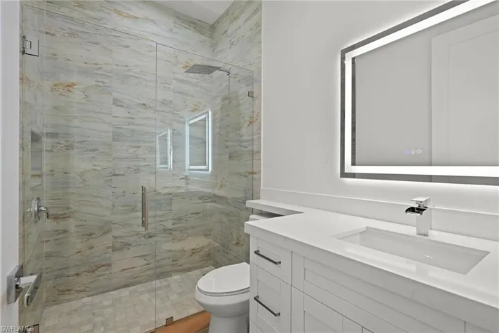 Bathroom with vanity, a shower with shower door, and toilet
