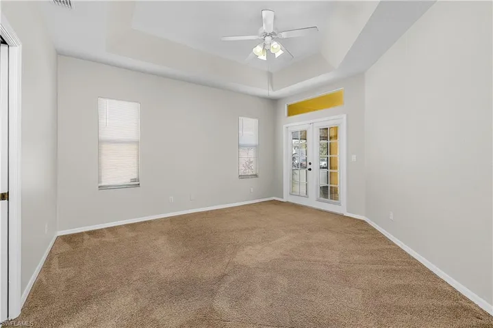 Primary Bedroom with french doors to Pool, a ceiling fan, and a raised ceiling