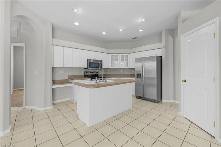 Kitchen with stainless steel appliances, white cabinetry, light countertops, glass fronted cabinets, and an island with sink