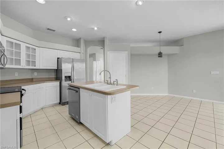 Eat in Kitchen with white cabinetry, glass insert cabinets, a kitchen island with sink, stainless steel appliances, and decorative light fixtures