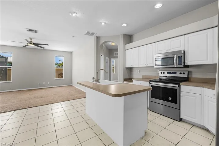 Kitchen with stainless steel appliances, arched walkways, open floor plan, and white cabinetry