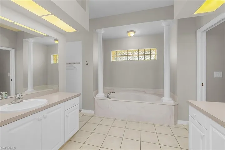 Full bathroom with dual vanities, a garden tub, ornate columns, and light tile patterned floors