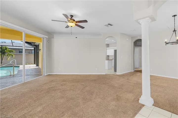 Unfurnished living room with sliders to pool, ceiling fan, decorative columns, and arched walkways