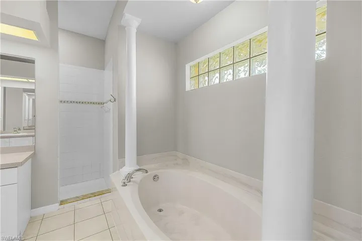Bathroom featuring a bath, vanity, Huge Walk- in tiled shower, ornate columns, and light tile patterned flooring