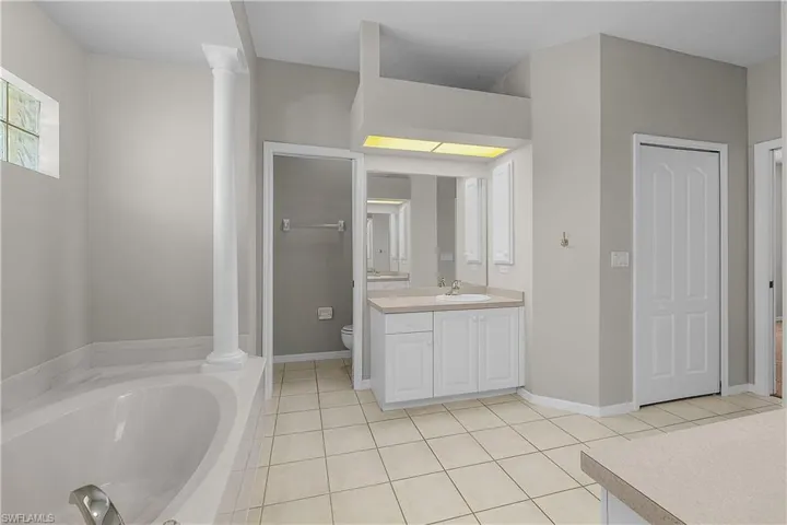 Bathroom featuring a garden tub, vanity, Private commode, decorative columns, and light tile patterned floors
