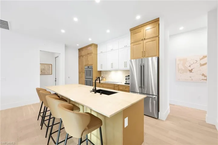 Kitchen with stainless steel appliances, light wood finished floors, a center island with sink, light brown cabinets, and recessed lighting
