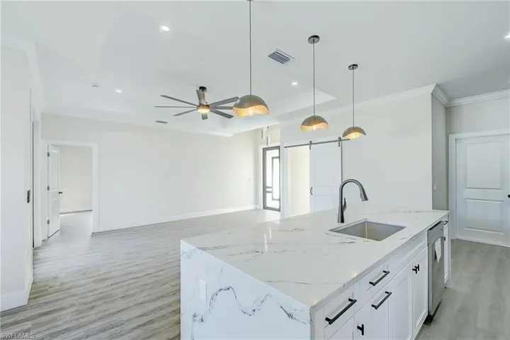 Kitchen featuring a barn door, light stone counters, a center island with sink, decorative light fixtures, and white cabinetry
