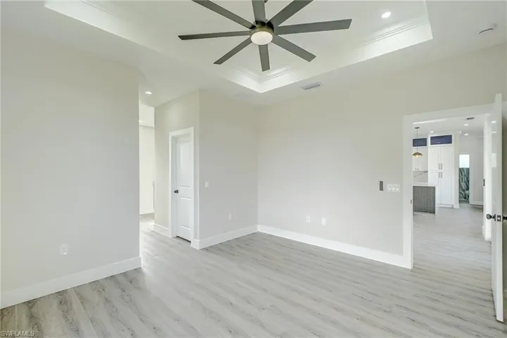 Spare room with a raised ceiling, recessed lighting, light wood finished floors, ornamental molding, and ceiling fan