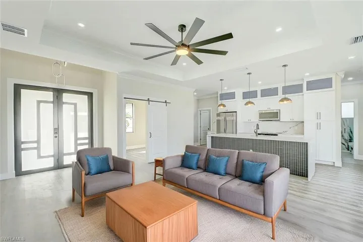 Living area featuring plenty of natural light, crown molding, a barn door, a raised ceiling, and recessed lighting. Staged picture