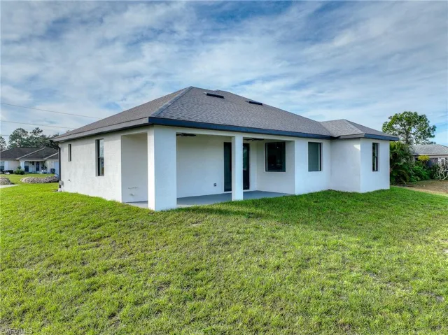 Back of property with stucco siding, a yard, a shingled roof, and a patio area