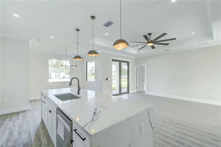 Kitchen featuring white cabinetry, light stone counters, pendant lighting, light wood-type flooring, and plenty of natural light