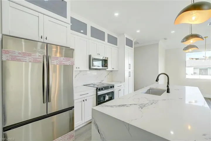 Kitchen featuring appliances with stainless steel finishes, light stone counters, white cabinetry, glass insert cabinets, and crown molding