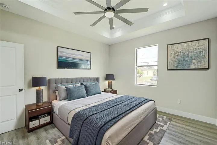 Bedroom featuring ornamental molding, wood finished floors, a tray ceiling, a ceiling fan, and recessed lighting