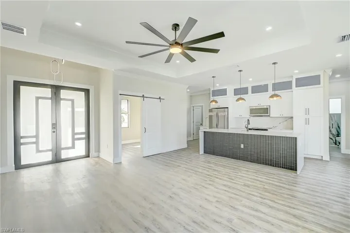 Unfurnished living room with a barn door, ornamental molding, a raised ceiling, light wood-style floors, and recessed lighting
