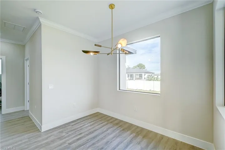 Empty room featuring crown molding, light wood-type flooring, and a chandelier