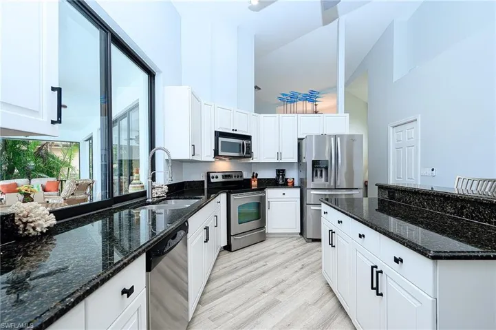 Kitchen with white cabinetry, light wood-type flooring, dark stone counters, stainless steel appliances, and sink