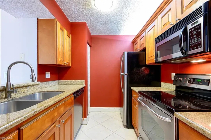 Kitchen with light stone counters, a textured ceiling, stainless steel appliances, sink, and light tile patterned floors