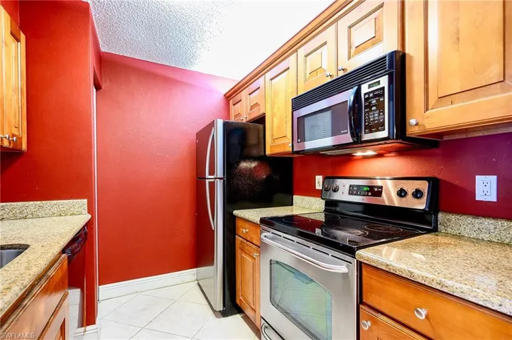 Kitchen featuring light stone countertops, light tile patterned floors, a textured ceiling, and appliances with stainless steel finishes