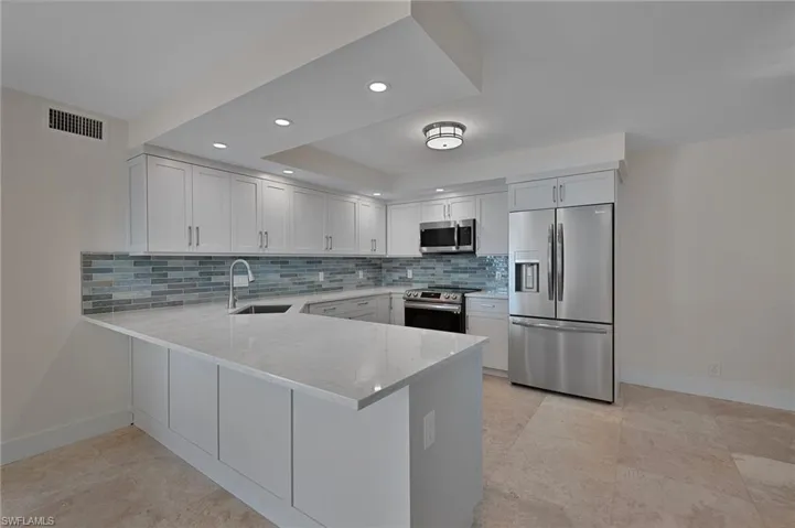 Kitchen with light stone counters, a sink, stainless steel appliances, a peninsula, and visible vents