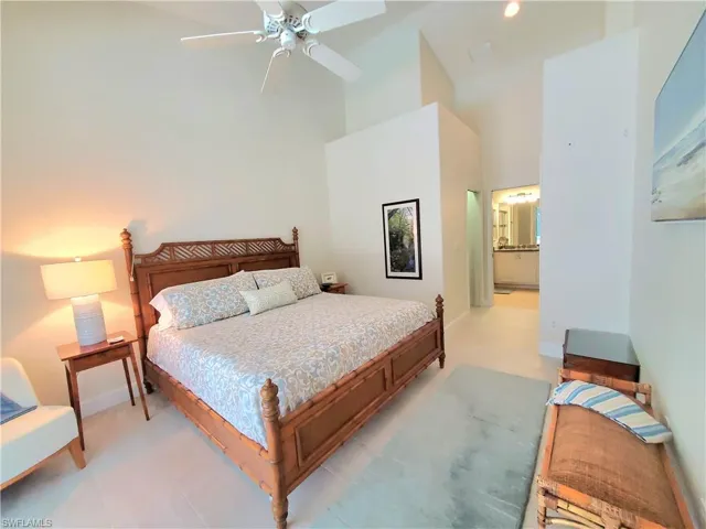 Tiled bedroom featuring high vaulted ceiling, ensuite bath, and ceiling fan