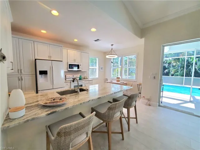 Kitchen featuring white appliances, light stone counters, hanging light fixtures, a breakfast bar, and white cabinets