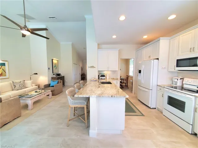 Kitchen with white cabinetry, white appliances, a kitchen bar, ceiling fan, and light tile floors