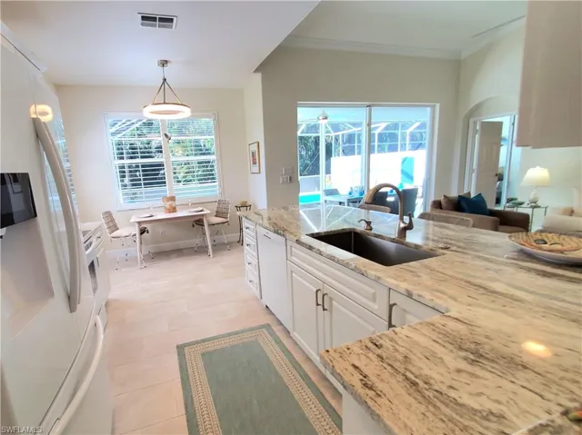 Kitchen featuring decorative light fixtures, light stone counters, white cabinets, sink, and white appliances