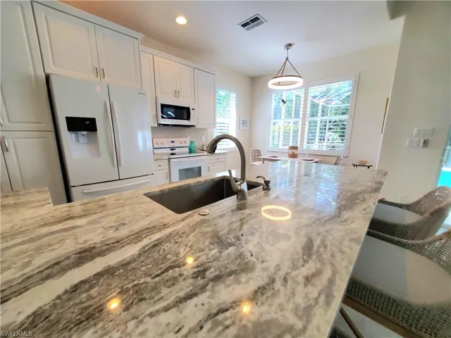 Kitchen featuring white appliances, white cabinets, light stone counters, decorative light fixtures, and sink