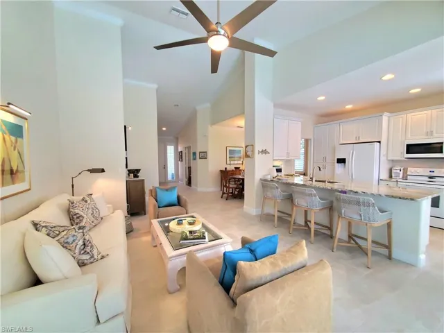 Living room with light tile flooring, ceiling fan, ornamental molding, high vaulted ceiling, and sink