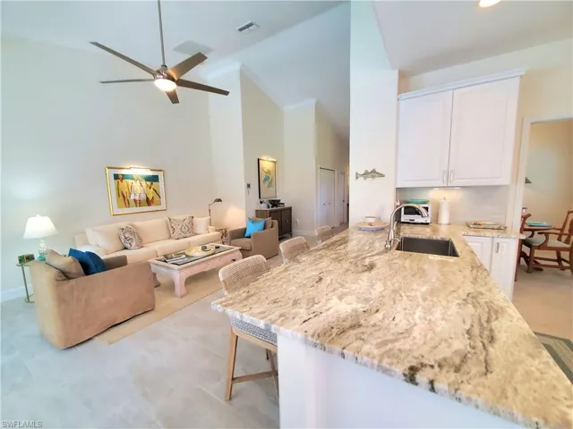 Kitchen with white cabinetry, a breakfast bar, high vaulted ceiling, light tile flooring, and ceiling fan