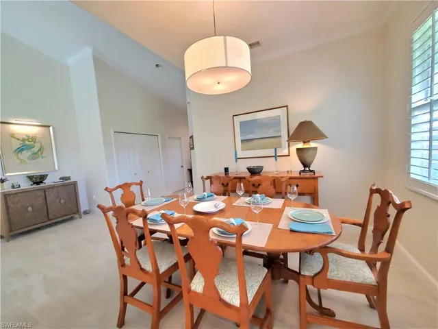 Carpeted dining space featuring plenty of natural light, vaulted ceiling, and crown molding