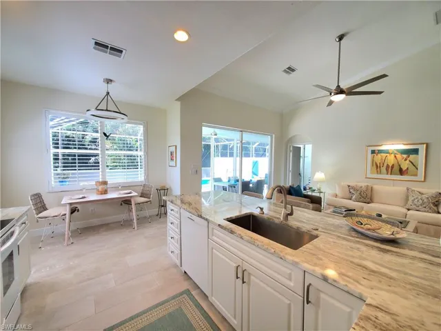 Kitchen featuring white dishwasher, white cabinets, light stone counters, decorative light fixtures, and sink