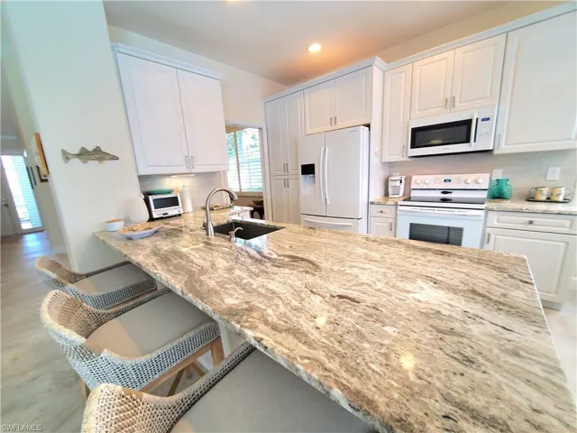 Kitchen with tasteful backsplash, a breakfast bar area, white cabinetry, sink, and white appliances